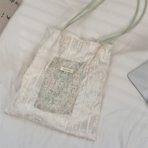 Detail of off-white tote bag with floral lace patch and green rope handle handles