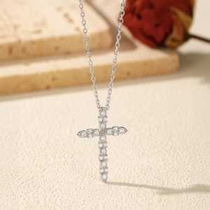 Silver D color moissanite cross necklace with sparkling stones on a beige background