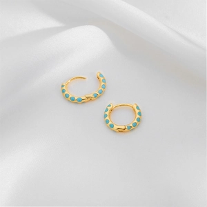 Detail of gold hoops with turquoise enamel inlay placed on white silk fabric background