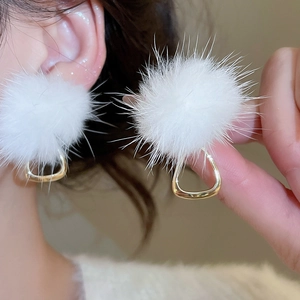 Detailed view of white pompom earrings with gold geometric accents worn by a model