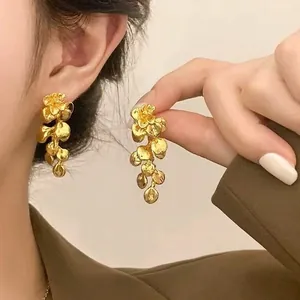 Detailed view of elegant long gold floral petal earrings with matte finish on a model