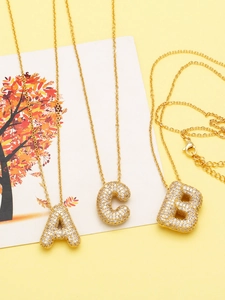 Detail of gold letter necklaces A, B, C with sparkling zircon pavé on a yellow surface