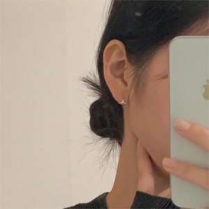 Close-up of minimalist silver star-shaped earring worn on ear with mirror finish