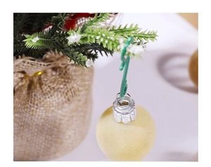 Close-up of a green S-shaped plastic hook hanging a yellow glitter Christmas ball ornament