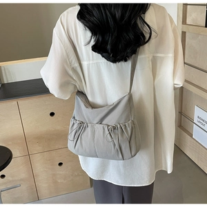 Detail of light gray nylon crossbody bag with drawstring pockets on back of a model
