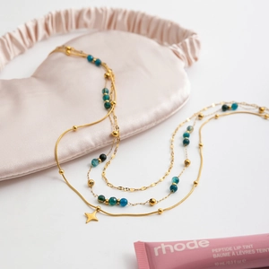 Détail d'un collier doré triple rang avec pendentif étoile et perles de pierre bleue