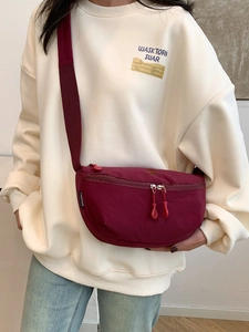 Bolso bandolera de nailon rojo oscuro con correa ajustable sobre sudadera blanca casual