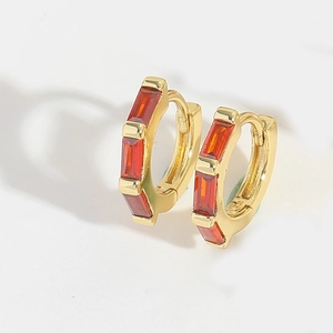 Detail view of gold earrings with three red rectangular cubic zirconia stones set in metal