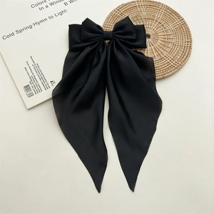 Detail of elegant black long tail ribbon bow hair clip on a minimalist magazine background