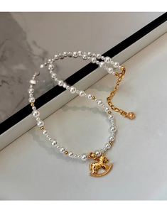 Macro detail of gold rocking horse pendant and lustrous white pearls on a necklace