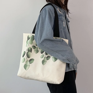 Close-up of white canvas tote bag with eucalyptus leaf print and black shoulder strap