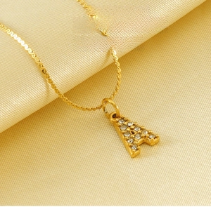 Dettaglio di una collana dorata con pendente a lettera A e cristalli su raso lucido