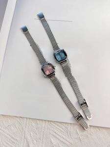 Close-up of square metal watches with pink and blue dials on an open vintage book