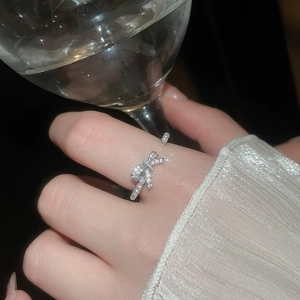 Detail of silver bow ring with zircon and pearls worn on hand with a wine glass