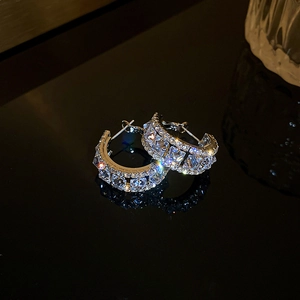 Detailed close-up of C-shaped silver earrings with square-cut sparkling zircons