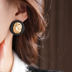 Close-up of a model wearing round gold hammered metal earrings with black outer edges