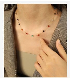 Detail of a delicate gold chain necklace with colorful beads worn on a model's neck