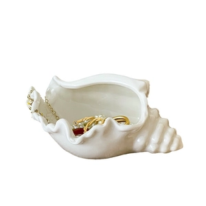 White ceramic conch shell jewelry tray for organizing rings and necklaces on table