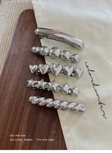 Detail of five silver metal hair clips with varied textures on wood and canvas background