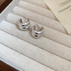 Macro shot of polished silver double-layered C-shaped earrings in a beige velvet jewelry box