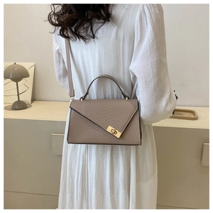 Detail of warm beige crocodile embossed leather bag with gold hardware lock closure