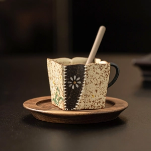 Handcrafted ceramic espresso cup with daisy pattern, wooden coaster, and stirring spoon
