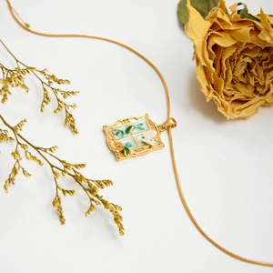 Vintage gold necklace with green window pendant and white flowers on white background