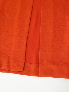 Detailed close-up of orange satin fabric showing subtle texture and rolled hem stitching detail