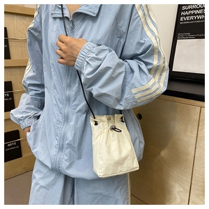 Detail of beige nylon drawstring bucket bag showing compact size and sleek shoulder strap