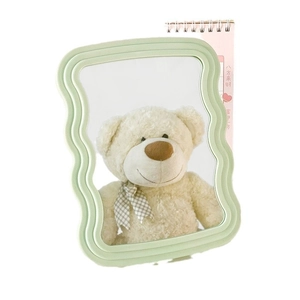 Light green wave-shaped vanity mirror with folding stand and clear reflection on white background