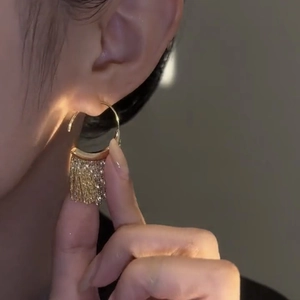 Macro shot of gold C-shaped earrings with long delicate flowing metal tassels