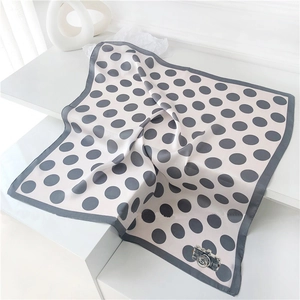 Detailed close-up of white silk scarf featuring grey polka dots and camera motif