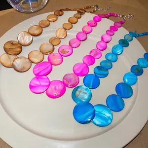 Shell beaded necklaces in brown, rose red, and peacock blue on a white ceramic plate