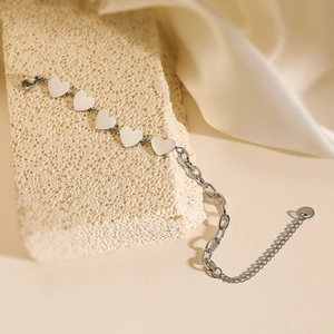 Elegant silver stainless steel heart charm bracelet on textured beige stone and silk