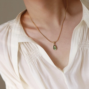 Close-up of a teardrop green gemstone pendant on a gold-plated snake chain necklace