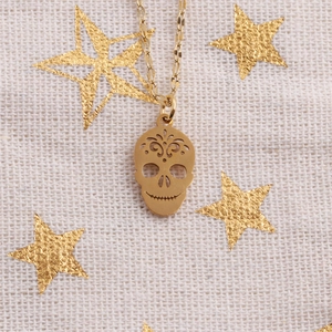 Macro detail of golden stainless steel sugar skull pendant with floral cutouts