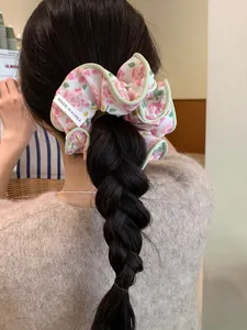 Floral scrunchie with pink flowers and green edges on a model's braided hairstyle