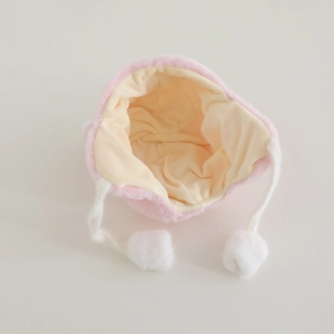 Close-up of pink plush baby hat with soft beige lining and white fuzzy pom-pom ties