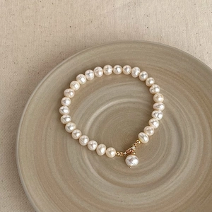 Baroque natural pearl bracelet with golden clasp on a ceramic plate, elegant jewelry detail