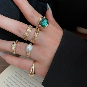 Detail of gold geometric rings set with green emerald and teardrop stones on model