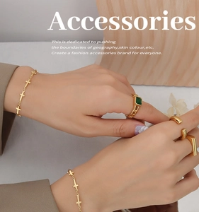 Detailed view of layered 18K gold plated cross bracelets and emerald cut rings on a hand