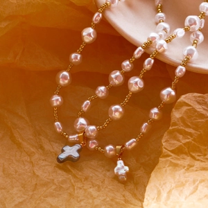 Détail macro de colliers en perles baroques avec pendentifs croix sur texture orange