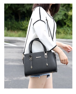 Detail of black pebbled faux leather handbag with metal hardware and shoulder strap