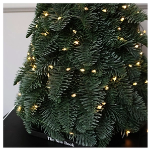 Close-up of warm LED lights on a lush green mini Christmas tree with book-style base