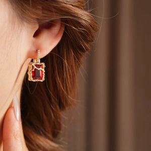 Détail de boucles d'oreilles carrées dorées avec zircon rouge et diamants sur un mannequin