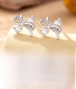 Macro detail of silver bow stud earrings featuring titanium steel and sparkling zircons