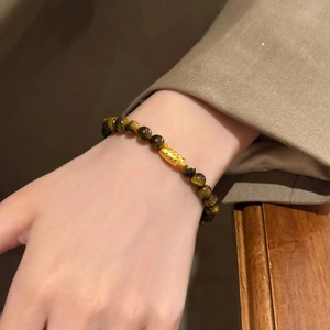 Detailed view of beaded tiger eye bracelet with a gold animal charm on a woman's wrist