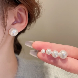 Detail showing various sizes of elegant white pearl stud earrings on ear and hand