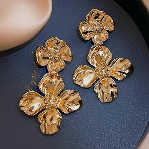 Détail de boucles d'oreilles fleurs dorées avec texture métallique sur plateau bleu
