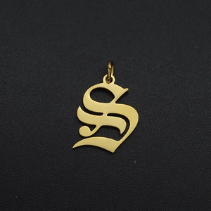 Close-up of golden stainless steel letter S pendant with ring on black texture